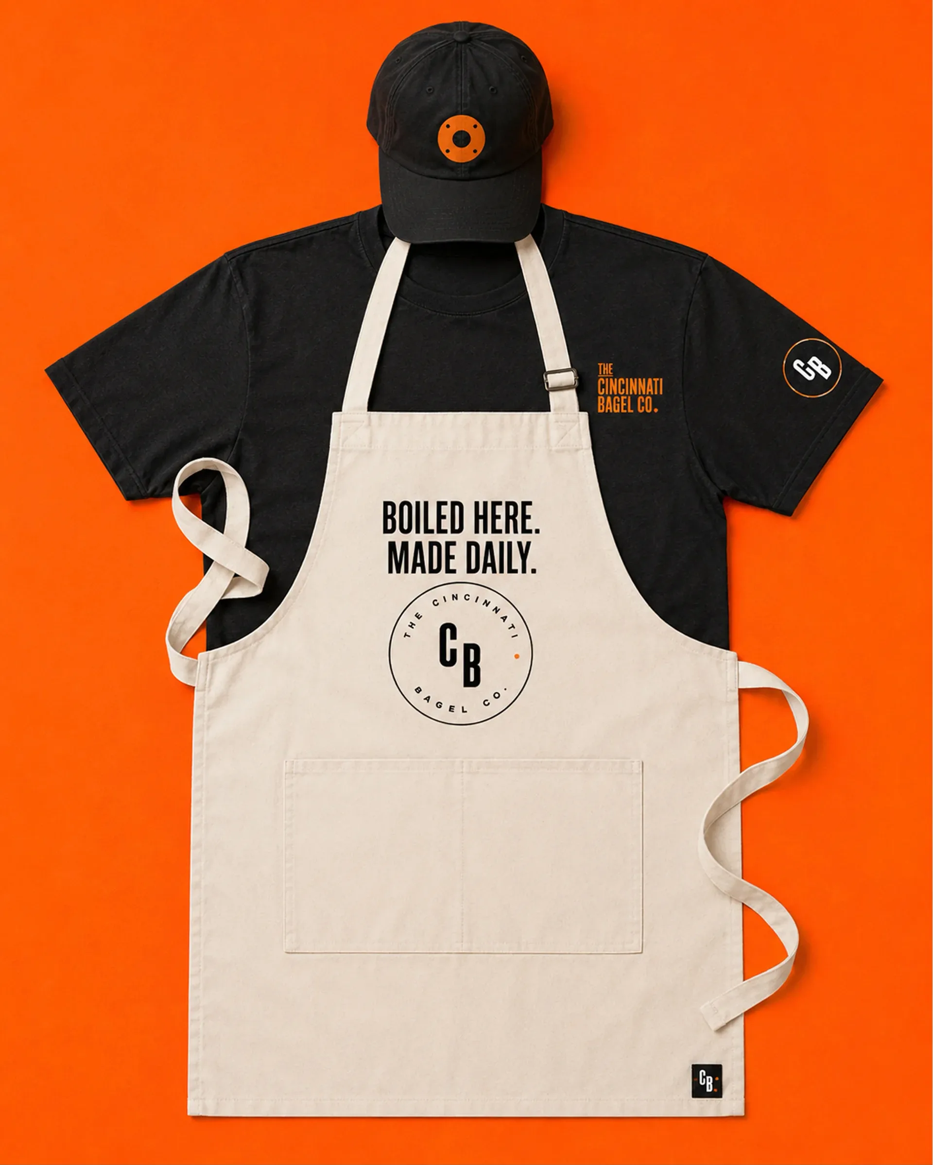 The Cincinnati Bagel Co. — Cincinnati Bagel Co. employee shirt and apron on an orange background