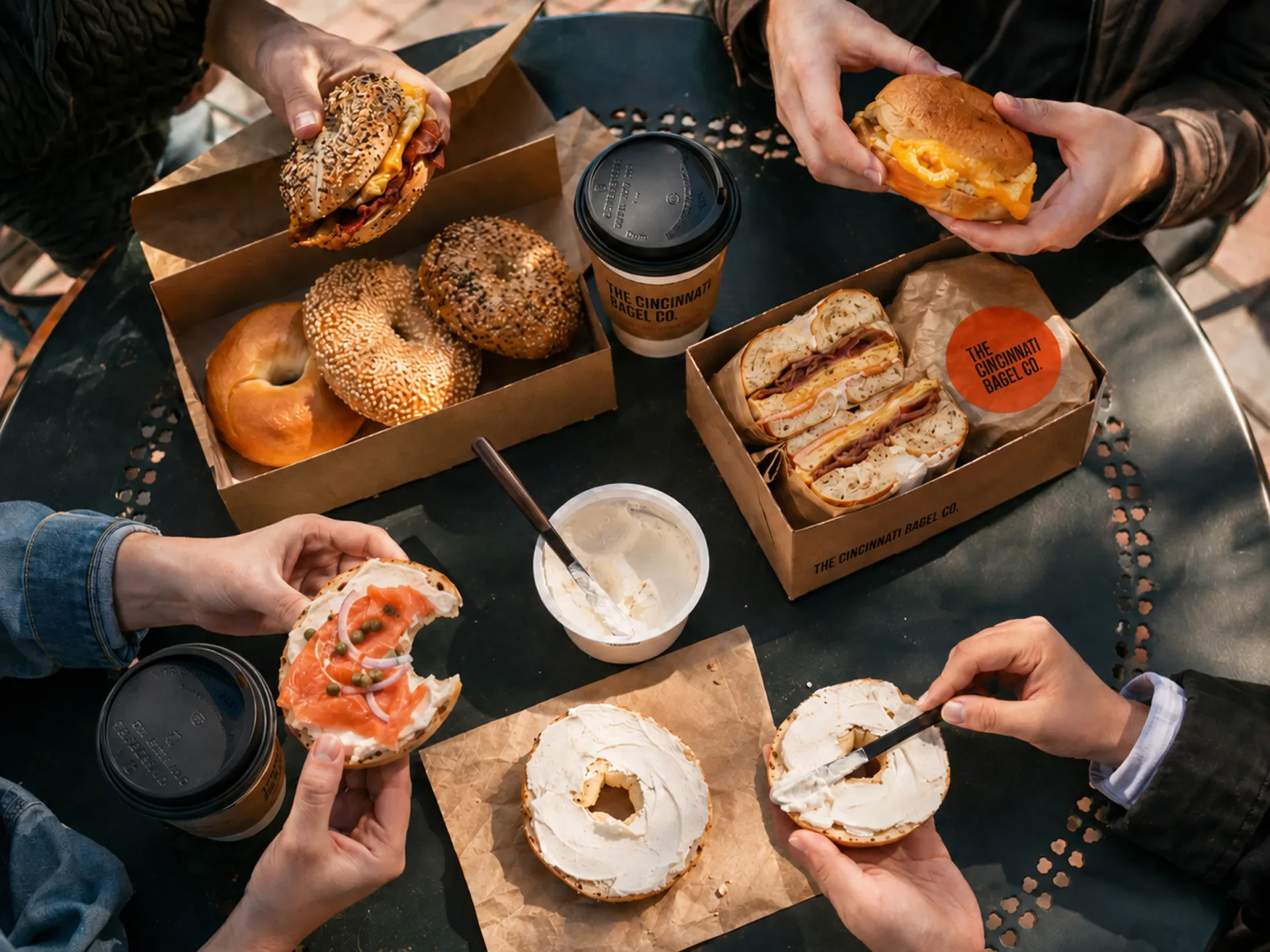 The Cincinnati Bagel Co. — People eating Cincinnati Bagel Co. breakfast together at a warm shop table