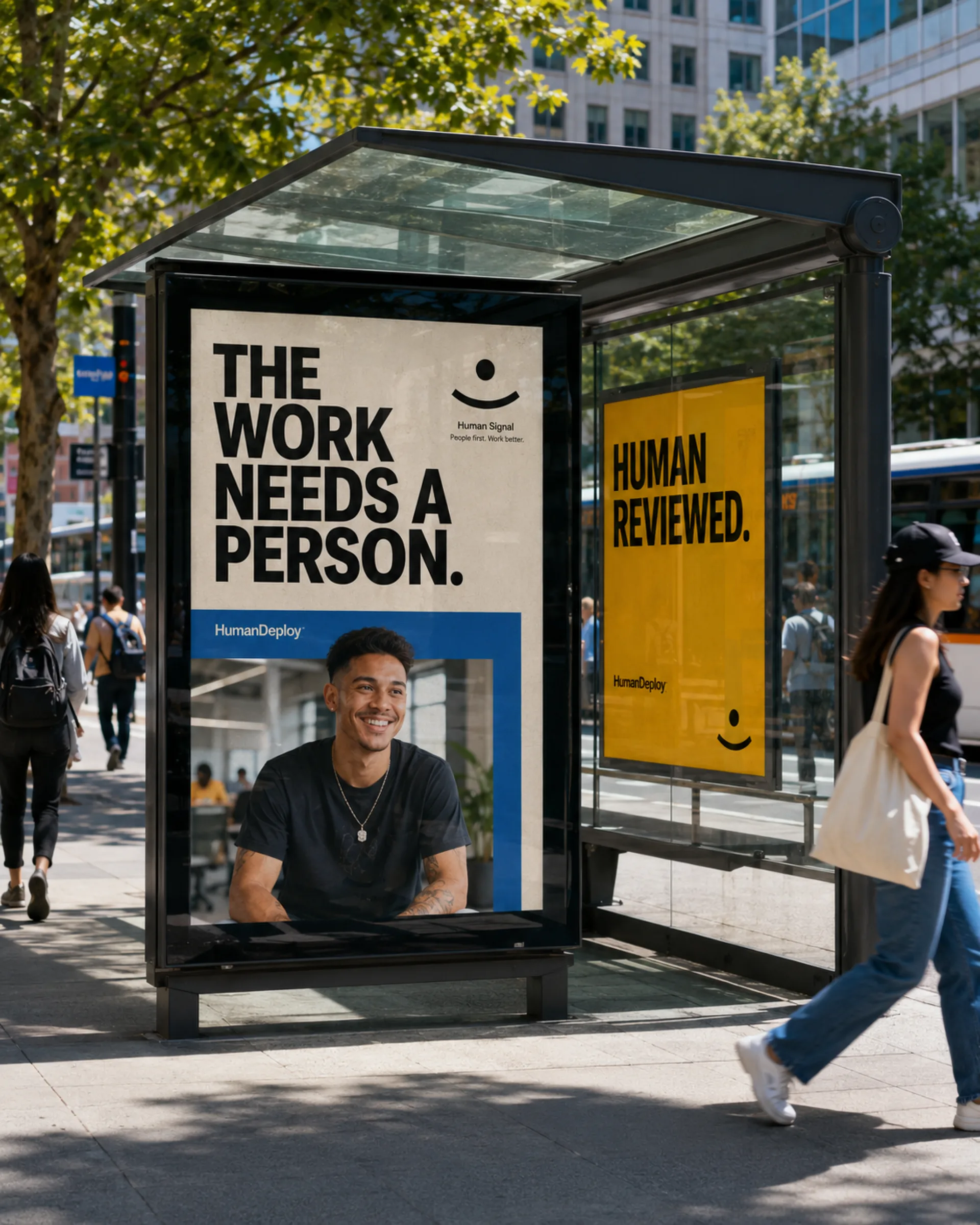 HumanDeploy — A sunlit city bus shelter carrying two HumanDeploy posters — 'THE WORK NEEDS A PERSON.' over a portrait beside a yellow 'HUMAN REVIEWED.' panel — as a pedestrian passes