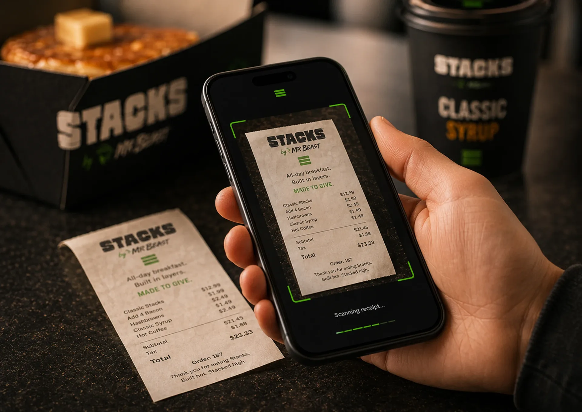 Stacks — Phone showing a Stacks app order screen beside a printed receipt, pancakes, syrup, and coffee