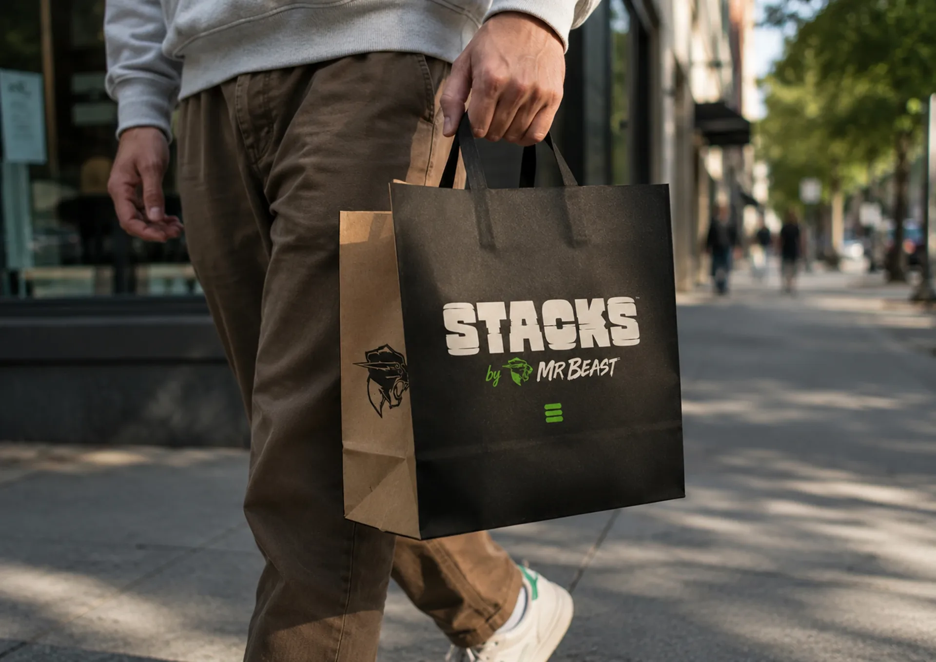 Stacks — Person carrying a black and kraft Stacks by MrBeast takeaway bag on a city sidewalk