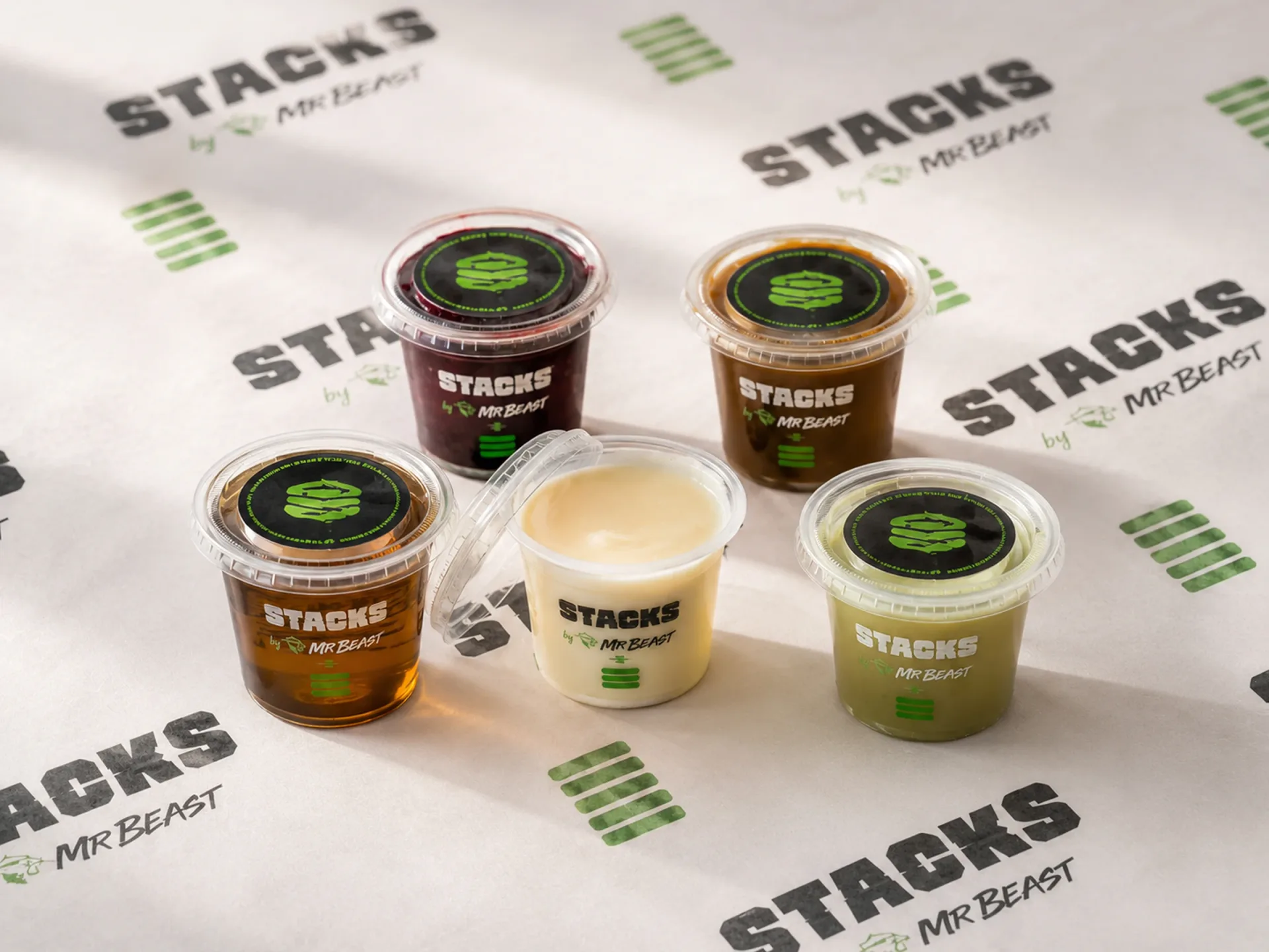 Stacks — Stacks branded sauce and topping cups arranged on repeated Stacks wrap paper